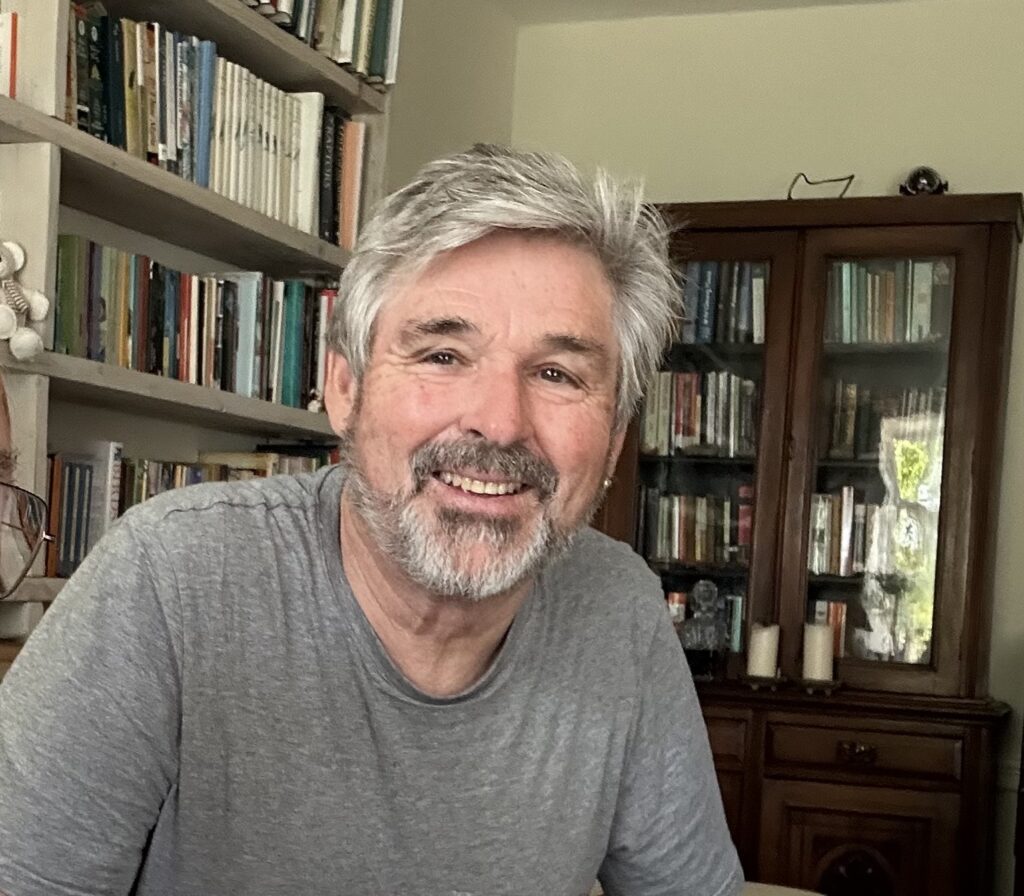Nigel Middleton.  Smiling man sitting in front of books.